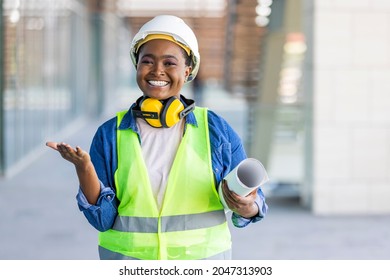 Portrait Of Woman Engineer At Building Site Looking At Camera With Copy Space. Mature Construction Manager Standing In Yellow Safety Vest And White Hardhat With Crossed Arms. 