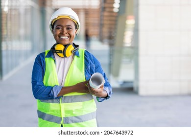 Portrait of woman engineer at building site looking at camera with copy space. Mature construction manager standing in yellow safety vest and white hardhat with crossed arms. 