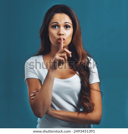 Portrait, woman and finger on lips for gossip secret with noise control, whisper and hush in studio. Female person, quiet emoji and silence for confidential news, privacy and mute by blue background