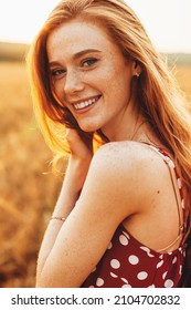Portrait of a woman with freckles in the wheat field looking at camera and smiling. Happy people. Beauty fashion model. Nature landscape. Wheat field.