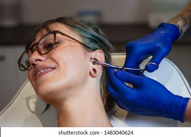 Portrait Of A Woman Getting Her Ear Pierced. Man Showing A Process Of Piercing Ear . Cleaning The Ear And Making It Steril. Ear Piercing Procedure