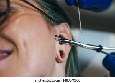 Portrait Of A Woman Getting Her Ear Pierced. Man Showing A Process Of Piercing Ear . Cleaning The Ear And Making It Steril. Ear Piercing Procedure