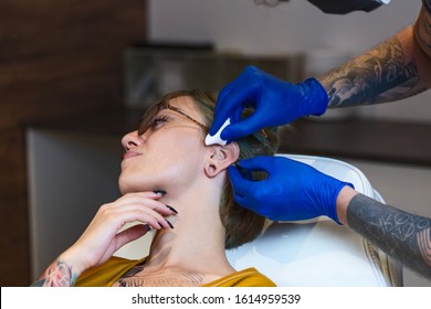 Portrait Of Woman Getting Her Ear Pierced. Man Showing A Process Of Piercing. Cleaning The Ear And Making It Sterile. Ear Piercing Procedure. Body Piercing. Beautiful Woman Getting Her Ear Pierced