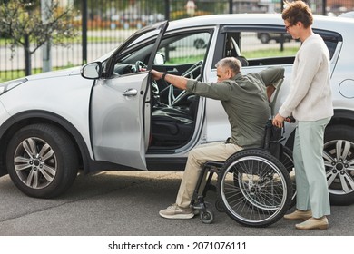 Portrait Of Woman Helping Man In Wheelchair Enter Car In Parking Lot Outdoors, Copy Space