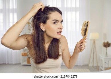 Portrait of woman in her 20s or 30s looking at her reflection with scared nervous expression as she notices bad signs like scalp dandruff, hair thinning, or hair falling out. Hair loss problem