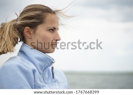 A portrait of a woman in her 20s/ 30s. Her hair is with highlights and it's on a ponytail. In the background, you could see a body of water -lake, river, pond, etc. 