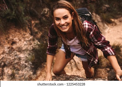 Portrait Of Woman Hiker Climbing A Rock And Looking At Camera Smiling. Female Hiking Over Extreme Terrain In Mountain.