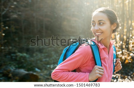 portrait of woman hiker with small backpack, wearing in pink fleece jacket, standing on pine woods background in the Carpathians woody mountains, Western Ukraine. happy smiling woman looking back at
