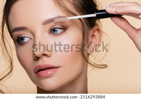 Portrait of woman holding brush of eyebrow gel isolated on beige