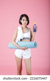 Portrait Of Woman Holding Exercise Mat Roll And Drinking Water Bottle, Holding Yoga Mat Roll On Pastel Pink Background.