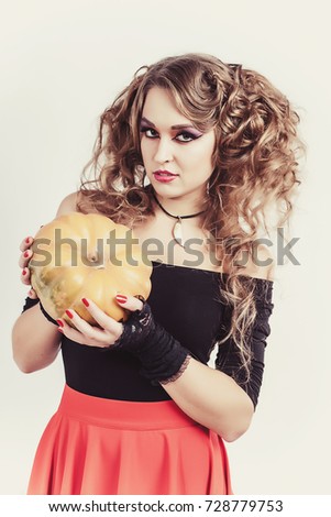 Portrait of woman holding in hands orange pumpkin isolated on gray background. Wearing black blouse and red skirt. Halloween celebration