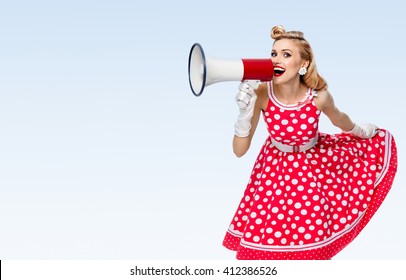 Portrait of woman holding megaphone, dressed in pin-up style red dress in polka dot and white gloves, on blue background, with blank copyspace area for text or slogan
