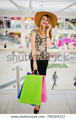 Portrait of a woman in leopard blouse, black skirt walking in shopping mall with bags and talking on the phone.