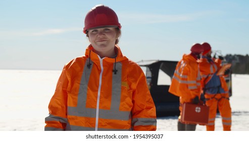 Portrait Of Woman Lifesaver Pin Hardhat Standing On Frozen Lake In Winter. Team Of Professional Lifeguards Patrolling Coast On Hovercraft