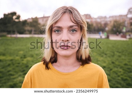 Portrait of a woman looking at camera outdoors with serious expression. Beautiful girl is cute. She looks unsmiling and attractive and confident. This caucasian female is posing sadness