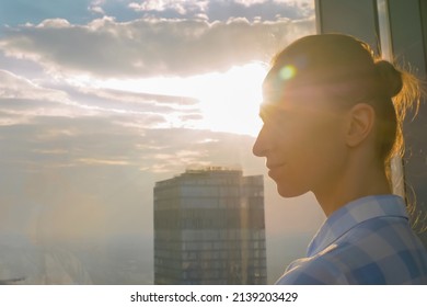 Portrait Of Woman Looking At Cityscape Through Window Of Skyscraper. Summer Time, Sunset, Sun Lens Flare. Success, Opportunity, Corporate, Sightseeing, Discover And Future Concept