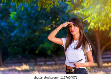 Portrait Of A Woman Looking Forward At Sunset Outdoor. Personal Development, Attainment Motivation Career Growth Concept. Portrait Of Beautiful Girl Tourist With Backpack Holding Travel Guide Book.