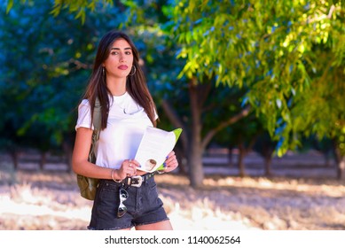 Portrait Of A Woman Looking Forward At Sunset Outdoor. Personal Development, Attainment Motivation Career Growth Concept. Portrait Of Beautiful Girl Tourist With Backpack Holding Travel Guide Book.