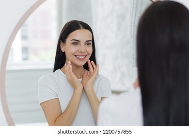 Portrait of a woman looking in the mirror at home, touching her face, skin, smiling, admiring