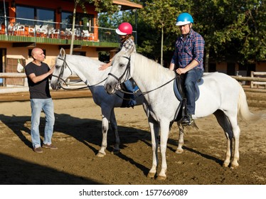 Portrait Of Woman And Man  With Trainer Riding Horse At Farm At Summer Day
