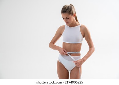 Portrait Of Woman Measuring Waist With Measuring Tape, Happy With Results Of Daily Fitness Workouts And Balanced Diet, Isolated On White. Toned Body, Flat Stomach, Abs