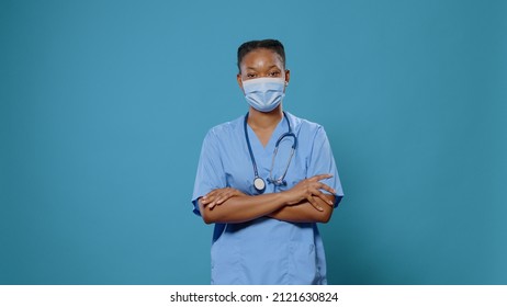 Portrait Of Woman Nurse With Crossed Arms Wearing Face Mask In Studio. Medical Assistant In Uniform Having Protection Against Coronavirus. Healthcare Specialist During Pandemic.