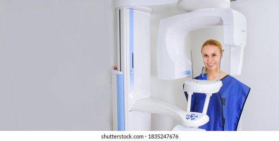 Portrait of a woman patient doing panoramic teeth x-ray orthopantomography in dental clinic in protective clothes and looking to the camera. Copy space for you text