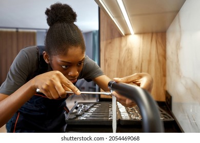 Portrait Of Woman Plumber At Work. African American Girl In Workwear Fixing Black Kitchen Tap. Modern Kitchen Interior And Toolkit On Background.