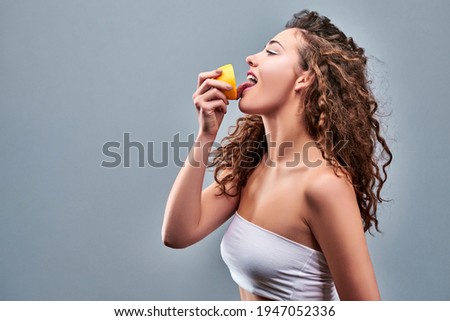 Portrait of woman promoting healthy eating. Beautiful young brunette woman holding fresh sliced lemon. Healthy eating lifestyle and weight loss concept. Studio grey background.