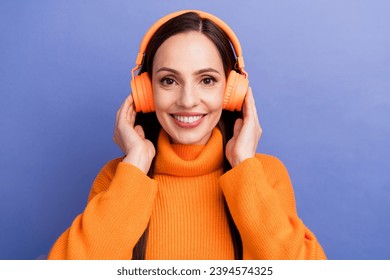 Portrait of woman in pullover touching her audio technology headphones sony for comfort listening music isolated on purple color background