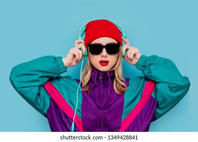 Portrait of a woman in red hat, sunglasses and suit of 90s with headphones on blue background.
