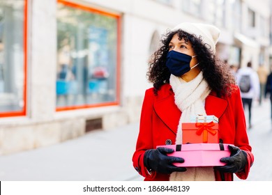 Portrait Of A Woman In Red Shopping Outside With Face Mask Holding Many Christmas Gifts And Presents Looking Up 