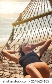 Portrait woman relaxing at sandy tropical beach on hammock. Lifestyle portrait happy smiling female resting in hammock. Summer tropical vacations concept. Travel and tourism. Copy space