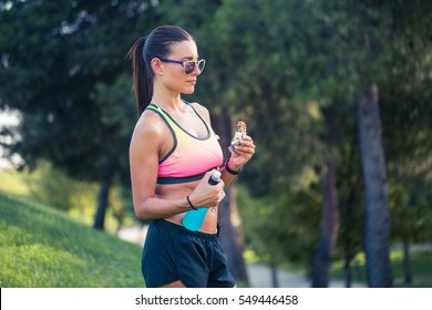 Portrait Of A Woman Runner Eating An Energy Bar, Outdoors In Park