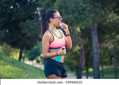 Portrait Of A Woman Runner Eating An Energy Bar, Outdoors In Park