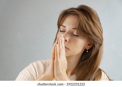 Portrait Of Woman, She Holds Hands In Praying Gesture, Isolated Over Grey Background, Has Sense Of Inner Peace.