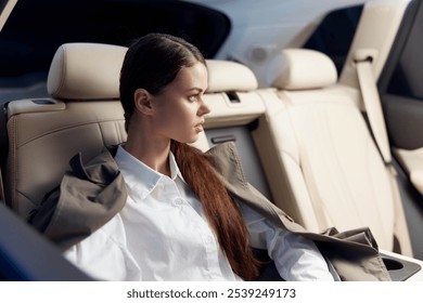 Portrait of a woman sitting in the back seat of a car, with her hands on her lap, gazing thoughtfully out of the window at the passing scenery - Powered by Shutterstock