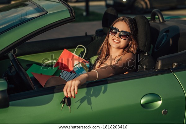 Portrait of woman sitting in the cabriolet car\
with shopping bags and\
smiling.