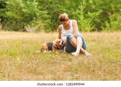 Portrait Of Woman Sitting On Grass Near Her Dog And Cat