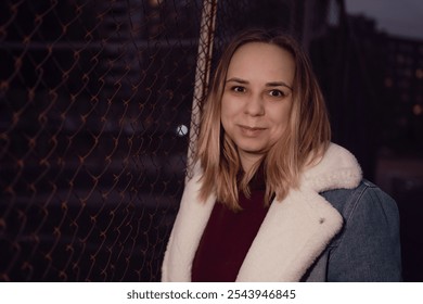 Portrait of a woman smiling near a chain-link fence during twilight in an urban setting. - Powered by Shutterstock