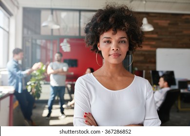 Portrait of woman standing in busy creative office looking at camera. Attractive female creative professional in design studio.