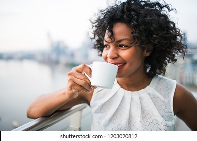 A portrait of a woman standing on a terrace, drinking coffee. - Powered by Shutterstock