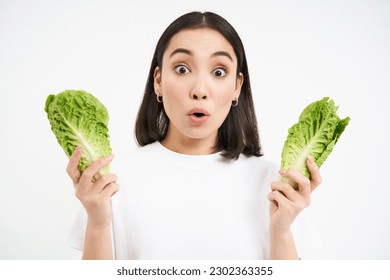 Portrait of woman with surprised face, holding cabbage, lettuce leaves and looks amazed, growing vegetables in own garden, white background. - Powered by Shutterstock