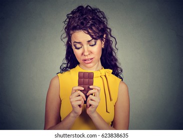 Portrait of a woman tired of diet restrictions craving sweets chocolate bar isolated on gray wall background. Human emotions. Nutrition concept. Feelings of guilt