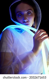 Portrait Of Woman In Transparent Raincoat And Flexible Blue And White Neon Tube Lights. Black Background                                        