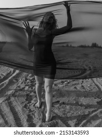 Portrait Of Woman Under Transparent Textile On Sand Dune. Girl Sneaking Through Fabric. Black And White