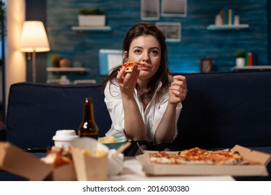 Portrait of woman watching comedy movie eating tasty delivery pizza slice relaxing on sofa in living room at night. Caucasian female enjoying takeaway food home delivered. Fastfood meal order