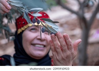 Portrait Of woman wearing palestinian traditional clothes in olive trees field holding branch in her hand with smile on her face - Powered by Shutterstock