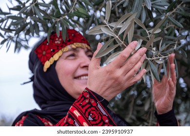 Portrait Of woman wearing palestinian traditional clothes in olive trees field holding branch in her hand with smile on her face - Powered by Shutterstock