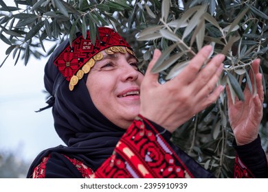 Portrait Of woman wearing palestinian traditional clothes in olive trees field holding branch in her hand with smile on her face - Powered by Shutterstock